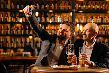 friends drinking beer and taking selfie with smartphone in bar or pub. male friendship - happy.