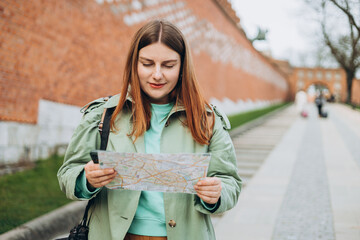 Wall Mural - Happy optimistic woman smiling confident holding city map at street. Attractive young female tourist is exploring new city. Traveling Europe in spring. Urban lifestyle banner