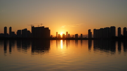 Wall Mural - the beautiful sunset view with the buildings' silhouette and orange color sky mirrored in the peacef