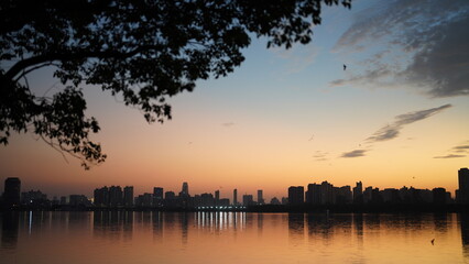 Wall Mural - the beautiful sunset view with the buildings' silhouette and orange color sky mirrored in the peacef