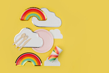 Wall Mural - Cute paper party plates in the shape of rainbow and clouds with cups for themed kids party. Birthday party decorations on yellow background. Set of holiday disposable tableware for party or picnic.