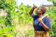image of african lady in a green field holding a farm tool- black lady in a farm looking to the sky with hole on the shoulder