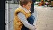 Little upset boy sitting next to metal fence feeling unhappy and lonely. Child depression, problems with bullying, victim in school, emigration, criminal and poverty