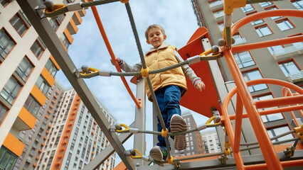 Wall Mural - Little smiling boy crossing rope bridge between two towers on outdoor kids playground