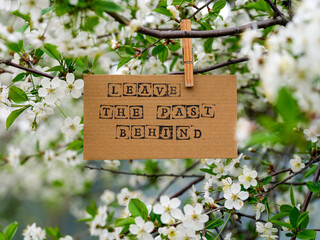 Wall Mural - A piece of cardboard with words Leave the Past Behind on it hanging on a cherry tree branch with blossoms using a wooden clothes pin.