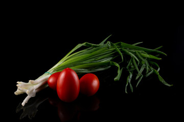 Fresh green onions and tomatoes on a black background