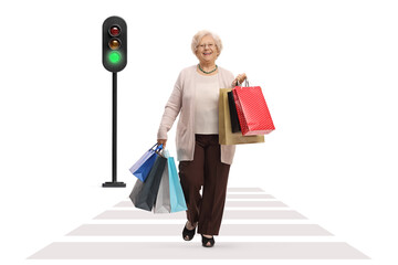 Wall Mural - Full length portrait of a happy mature woman with shopping bags walking at pedestrian crossing