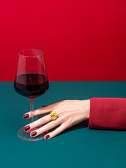 Cropped anonymous person in red clothes with well cared hand and manicured nails holding glass of wine over two color background. Wine shop, wine tasting, bar, wine list concept. Refreshment drink.