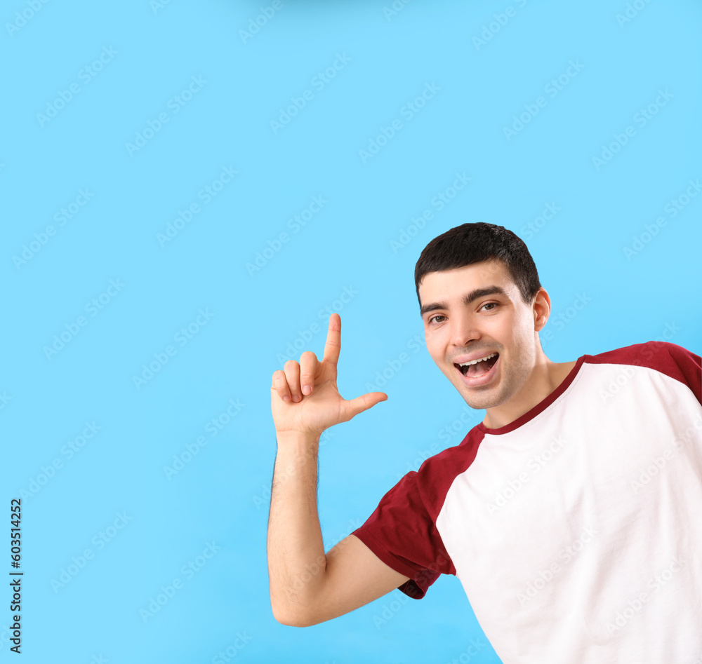 Young man showing loser gesture on blue background
