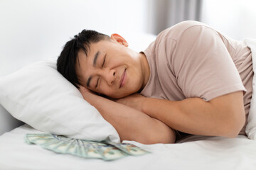 Asian man sleeping with bunch of cash dollars under pillow