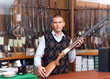 © JackF - Salesman standing behind counter at gun shop, showing double barreled hunting rifle