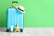 Leinwandbild Motiv Suitcase with beach accessories and starfishes near green wall