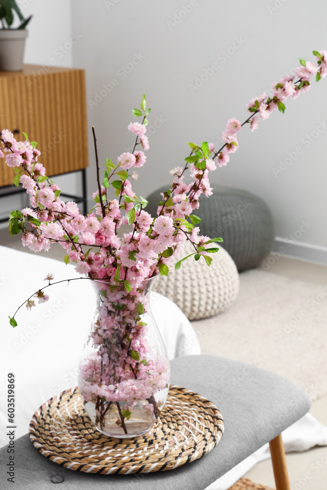 Vase with blooming sakura branches on bedside bench in interior of bedroom