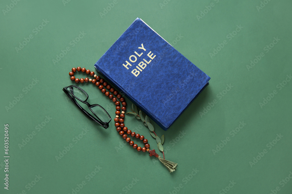 Holy Bible with eyeglasses and prayer beads on green background