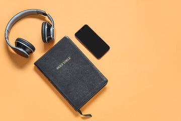 Wall Mural - Holy Bible with earphones and smartphone on orange background