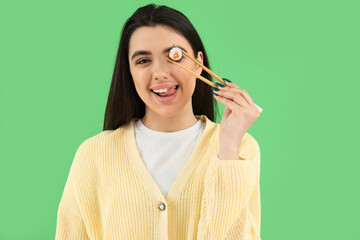 Canvas Print - Young woman with sushi roll on green background, closeup