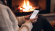 © jr-art - a woman is doing something on her smartphone in front of a burning fireplace. Generative AI