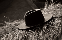 Black And White Photo Of A Cowboy Hat On A Hay Bale In A Barn