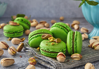 Wall Mural - Green colored pistachio macarons with pistachios and mint on gray wooden background