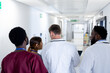 © wavebreak3 - Rear view of diverse group of doctors in discussion, walking in hospital corridor