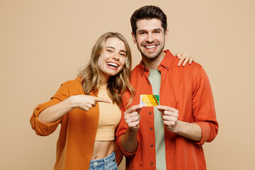 Canvas Print - Young couple two friends family man woman wear casual clothes hold in hand point index finger on mock up of credit bank card together isolated on pastel plain beige color background studio portrait.