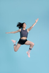 Determined, competitive sportswoman, jumping high up, stretching, exercising over blue background