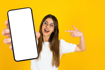 Mobile offer, excited caucasian lady pointing finger to smartphone in her hand for great mobile offer. Looking mobile phone with empty blank screen mockup. Isolated orange studio background.