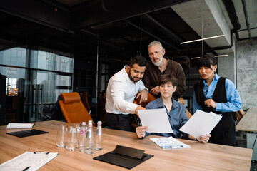 Wall Mural - Serious multiethnic colleagues checking documents behind boss back in office