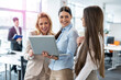 © Bojan - Beautiful multi-aged businesswomen standing in office hall, holding laptop and analyzing marketing data and company's growth, having consultation for business planning, strategy and financial budget.
