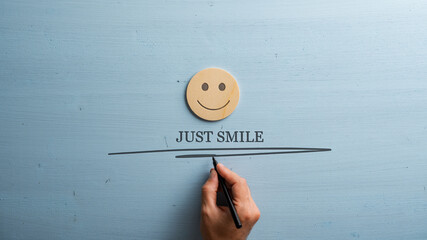 Male hand writing a Just smile sign under a wooden cut circle with a smiling face drawn on it