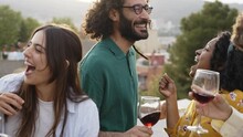 Multiracial group of friends dancing and drinking red wine at rooftop party - Happy multiethnic young people having fun outside on summer vacation 