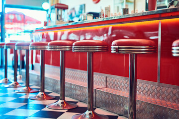 Trendy, vintage and retro interior in a diner, restaurant or cafeteria with funky decor. Booth, old school and chairs by a counter or bar in a groovy, vibrant and stylish old fashioned empty cafe.