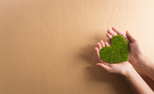 Hands Holding Green Heart On Brown Background. World Environment Day, Earth Day And Save Earth Concept.