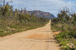 © Austockphoto - A long straight gravel road cutting through bush toward distant mountains