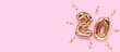 Banner with number 20 gold colored inflatable balloons with ribbons confetti on a pink background.