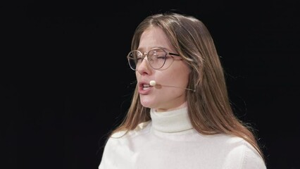 optimistic caucasian businesswoman using headset for motivational speech from black stage. professio