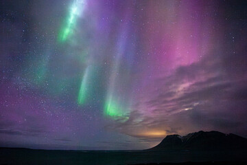 pink and green northern lights above the sea with silhouette hills in iceland