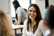 © ADDICTIVE STOCK - Generative AI image of cheerful young female looking at camera while sitting in office and speaking with anonymous colleagues against blurred office in daytime
