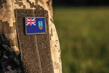 Close up millitary woman or man shoulder arm sleeve with Montserrat flag patch. Troops army, soldier camouflage uniform. Armed Forces, empty copy space for text
