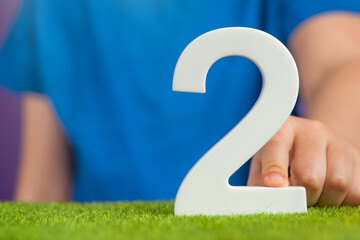 Fototapete - White number 2 in hand. The hand holding the number 2 symbolizes choice, partnership and duality, the choice between two alternatives, to combine the efforts of two people to achieve a common goal.