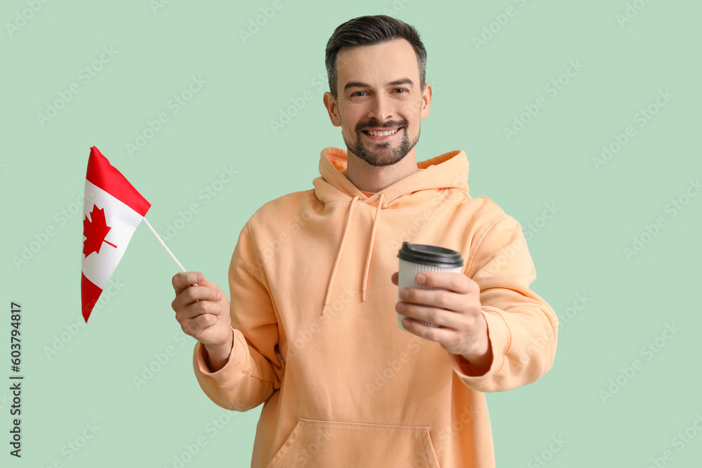 Handsome man with flag of Canada and coffee cup on green background