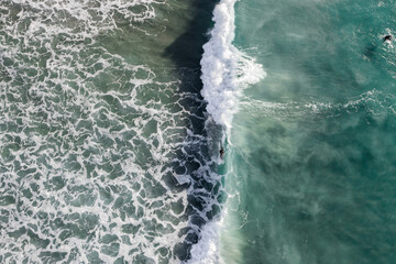 Canvas Print - Aerial view of a strong wave crashing with surfers nearby 