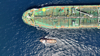 Aerial drone photo of huge crude oil tanker assisted by tug boat cruising open ocean deep blue sea