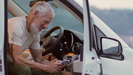 Wall Mural - Happy older man sitting in rv camper van using mobile phone. Smiling mature active traveler holding smartphone texting enjoying view and wireless internet in camping, booking campervan.