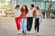 © CarlosBarquero - Photo of group of four young friends happily walking in city street. Smiling students laughing and having fun together on a sunny day. Erasmus cheerful classmate university people hugging together.