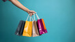 © Prasanth - Female hand holding many colorful shopping bags on blue background, template