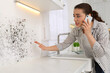 © New Africa - Mold removal service. Woman talking on phone and looking at affected wall in kitchen