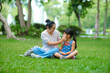 © Pornpimon - Mother and little daughter sitting on the grass together in the park. Mother having fun with her little daughter outdoors in green nature park. Happy family concept. Mother's Day