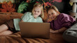 © TrueFrame Collective - Caucasian woman and her preteen daughter relaxing together on bed at home watching series online on laptop