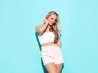 Wall Mural - Young beautiful smiling blond female in trendy summer shorts clothes. Sexy carefree woman posing near blue wall in studio. Positive model having fun. Cheerful and happy. Going crazy. In sunglasses